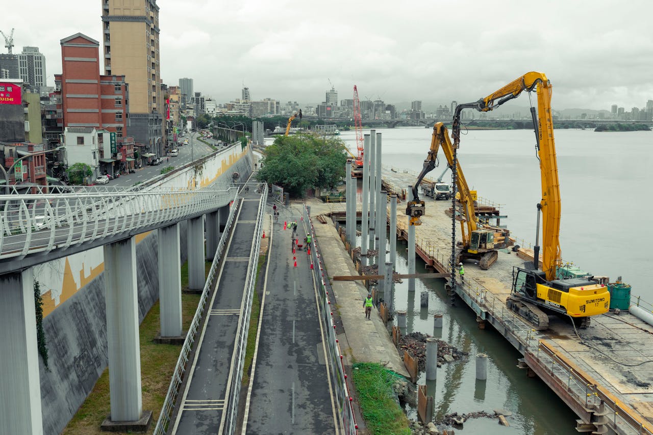 Aerial view of a construction site along a riverfront in Taipei, Taiwan, with machinery and workers.